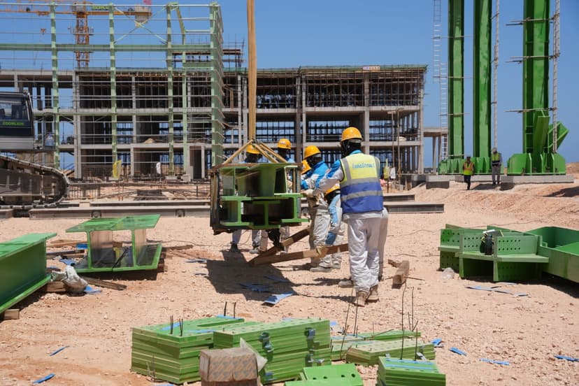 Workers in protective gear handling steel structures at a large construction site.