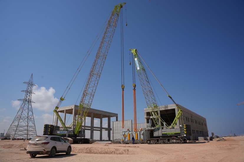 Two Zoomlion crawler cranes lifting heavy industrial equipment at a construction site.