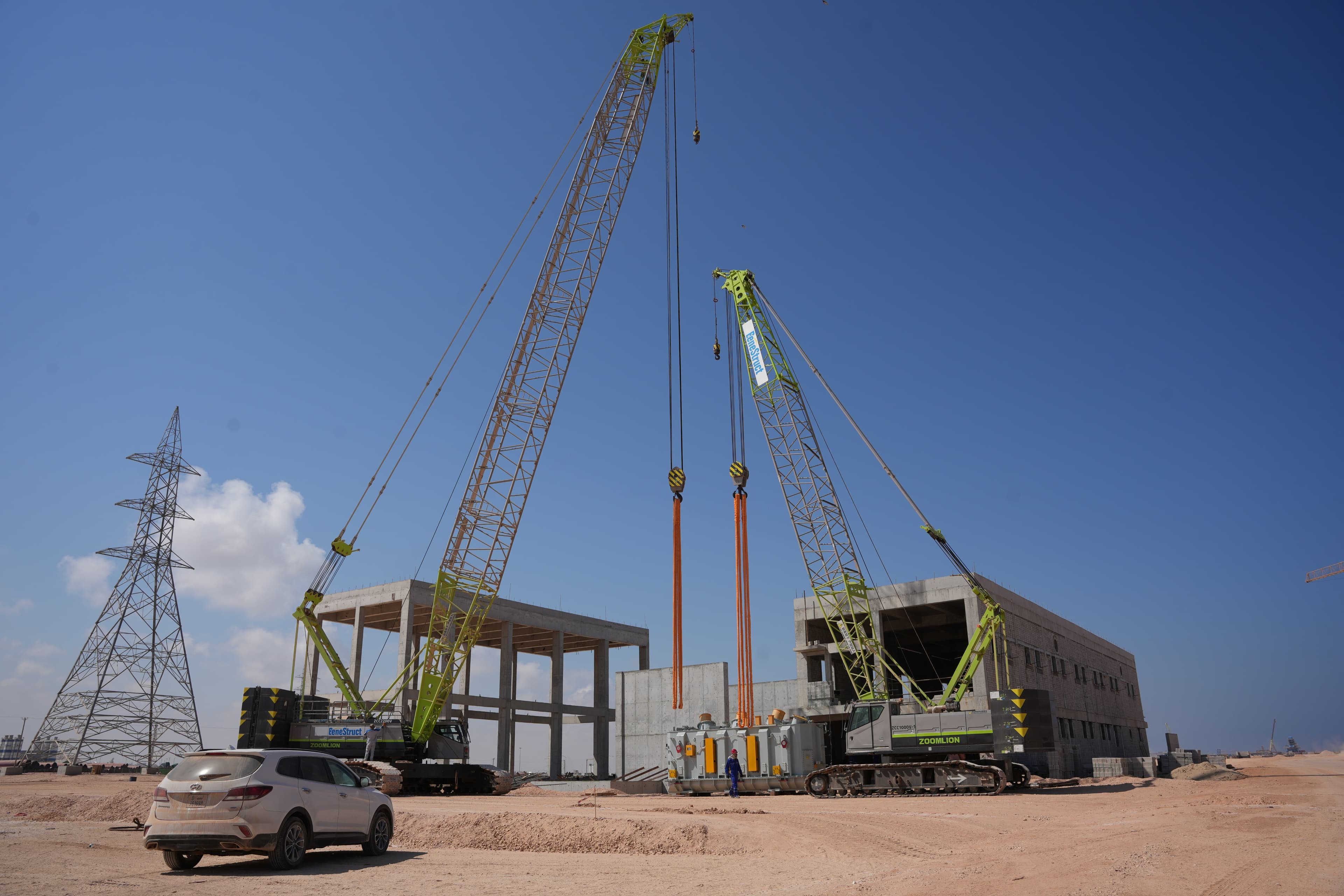 Two Zoomlion crawler cranes lifting heavy industrial equipment at a construction site.
