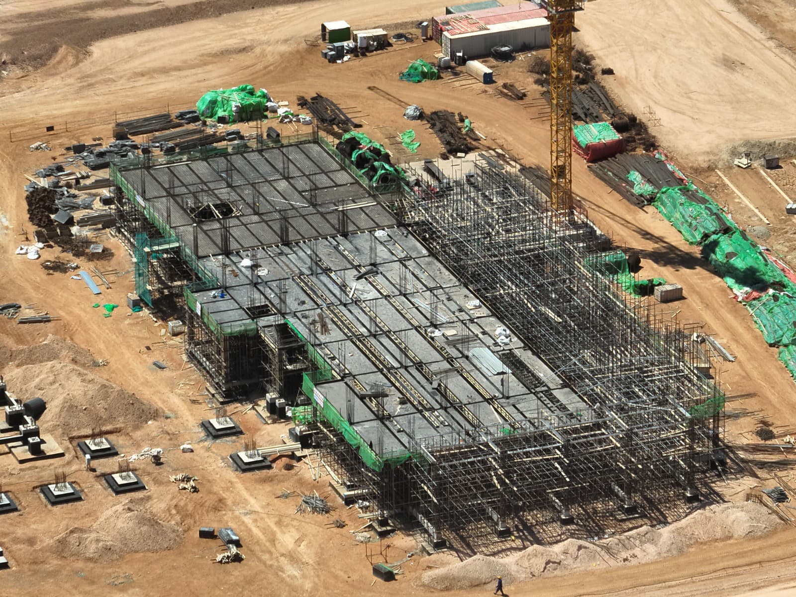Aerial view of active construction at the Benghazi steel complex showing cooling tower foundations and heavy machinery near the coastline.